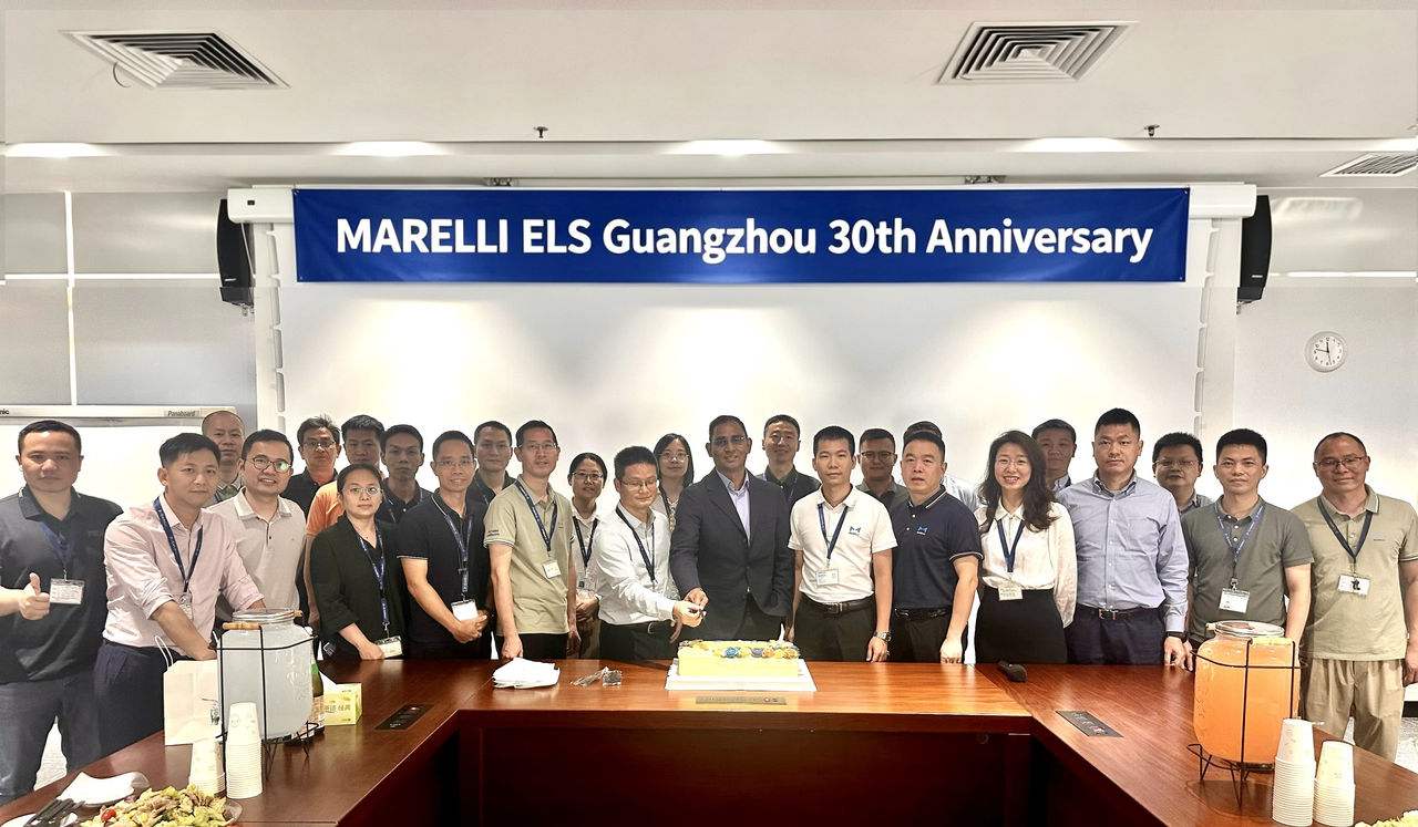 Group of employees celebrating Marelli ELS Guangzhou 30th anniversary with a cake under a blue banner.