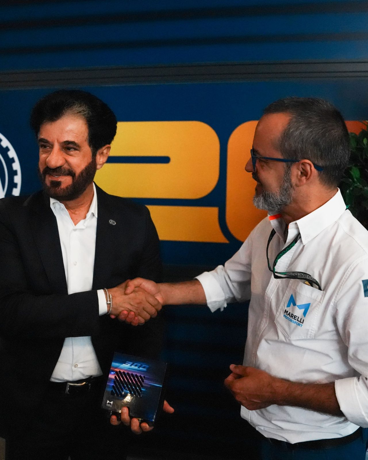 Two professionals shaking hands while holding a Marelli electronic component.