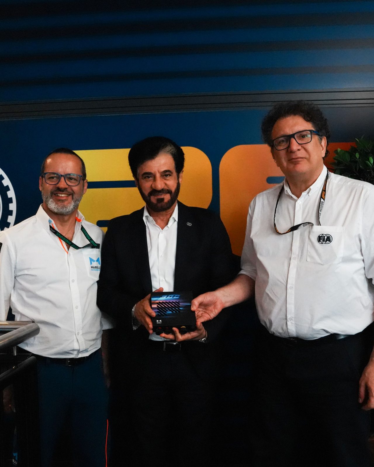 Three professionals presenting a Marelli electronic device at an event booth.