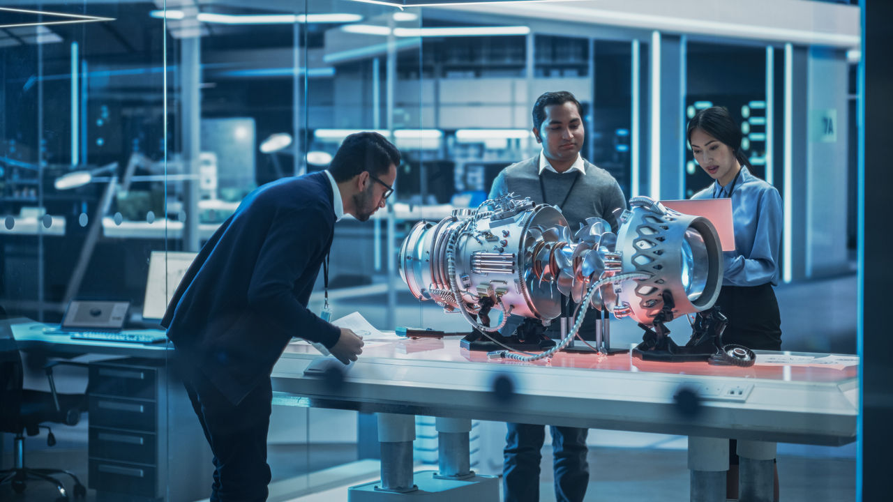 Software Developer, Project Manager and Machinery Operators Collaborate on a Prototype Turbine Engine, Standing with Laptop Computer in Scientific Technology Lab. Team Developing a New Electric Motor